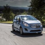 A light blue 2016 Chevy Spark EV is shown on a highway after visiting a used Chevy dealership.