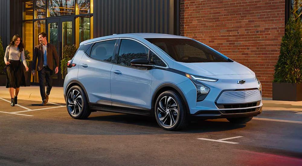 A light blue 2022 Chevy Bolt EV is shown parked near a brick wal.