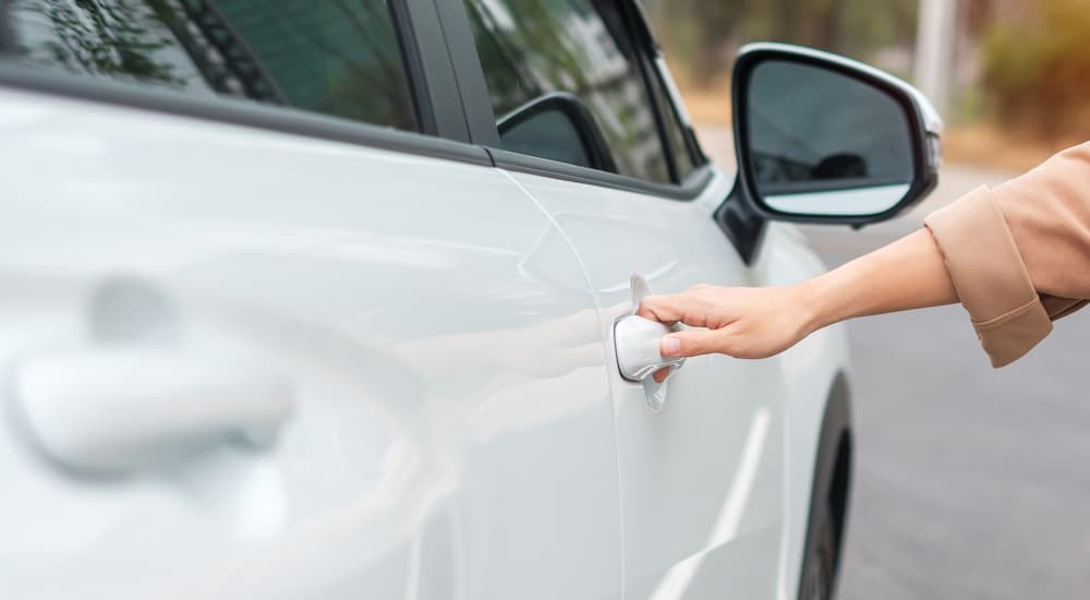 A person is shown opening a white car's door.