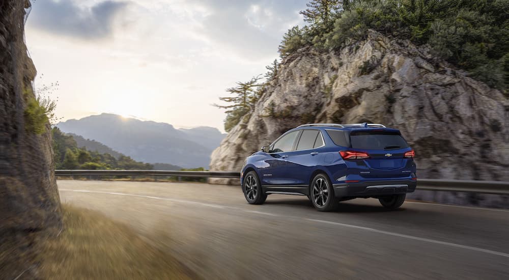 A blue 2023 Chevy Equinox is shown from the rear while driving.