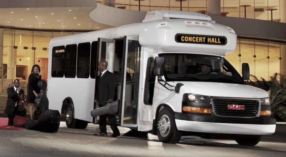 A white 2022 GMC Savana Cutaway 3500 is shown parked outside of a concert hall.