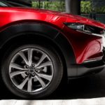 A close up shows the front end and passenger side wheel on a red 2022 Mazda CX-30.