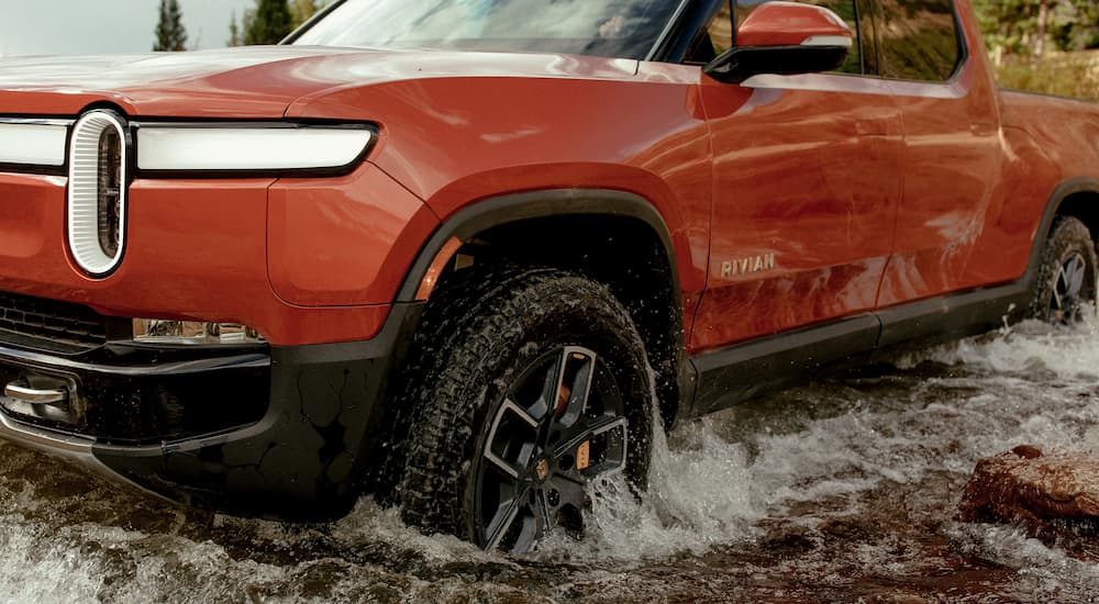 A red 2022 Rivian R1T is shown driving through a river.
