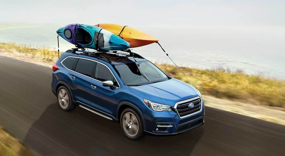 A blue 2022 Subaru Ascent Touring is shown driving next to a lake.