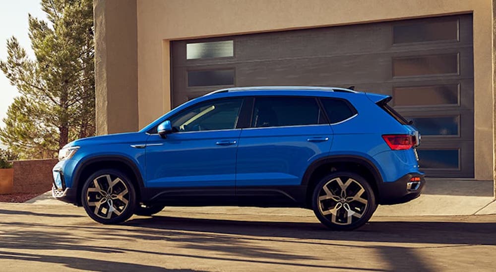 A blue 2022 Volkswagen Taos is shown from the side while parked in front of a garage during a 2022 Volkswagen Taos vs 2022 Mazda CX-30 comparison.
