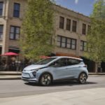 A popular Chevy Bolt for sale, a blue 2023 Chevy Bolt EV, is shown from the side after driving on a city street.