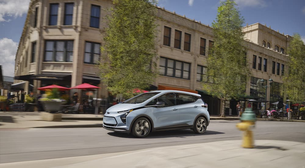 A popular Chevy Bolt for sale, a blue 2023 Chevy Bolt EV, is shown from the side after driving on a city street.