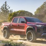 A red 2023 Chevy Colorado Trail Boss is shown from the front at an angle while driving off-road.