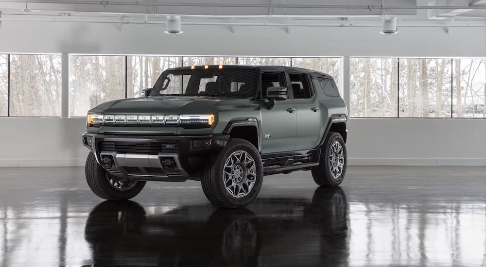 A green 2024 GMC Hummer EV is shown from the front at an angle while parked in a showroom.