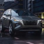 A grey 2023 Hyundai Tuscon is shown driving on a city street.