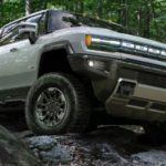 A green 2024 GMC Hummer EV is shown from the front while driving off-road.