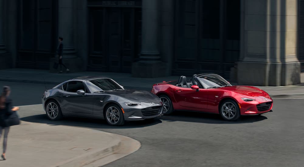A grey 2022 Mazda MX-5 Miata RF and red GT are shown driving on a city street.