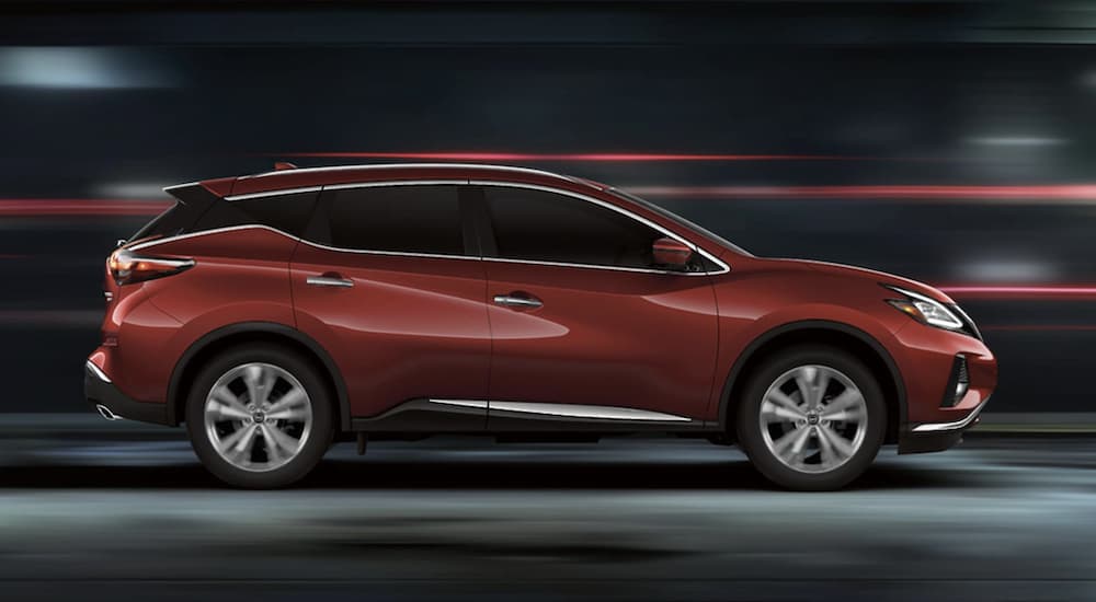 A red 2023 Nissan Murano for sale is shown driving from the side.
