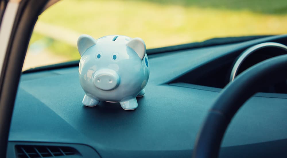 A white piggy bank is shown on a car dashboard.