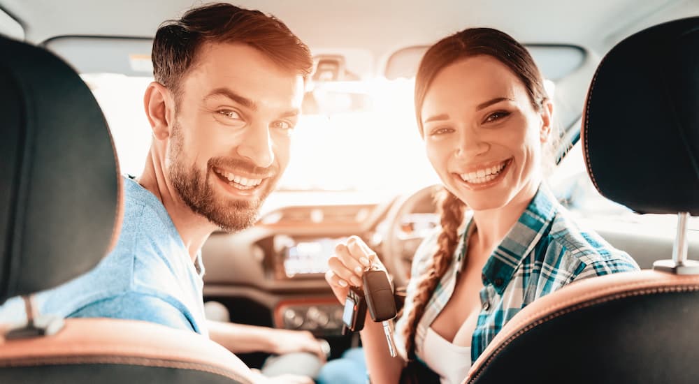 A couple is shown smiling in the front seat of a their vehicle.