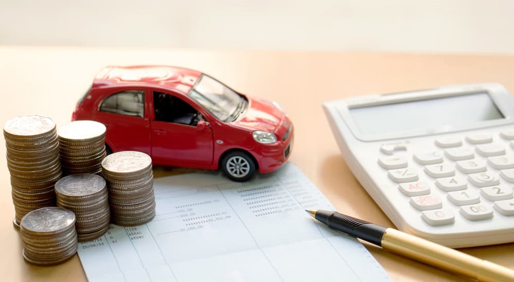 A red toy car is shown next to a pile of coins.