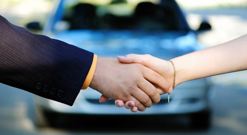 A car salesman is shown shaking hands with a customer.