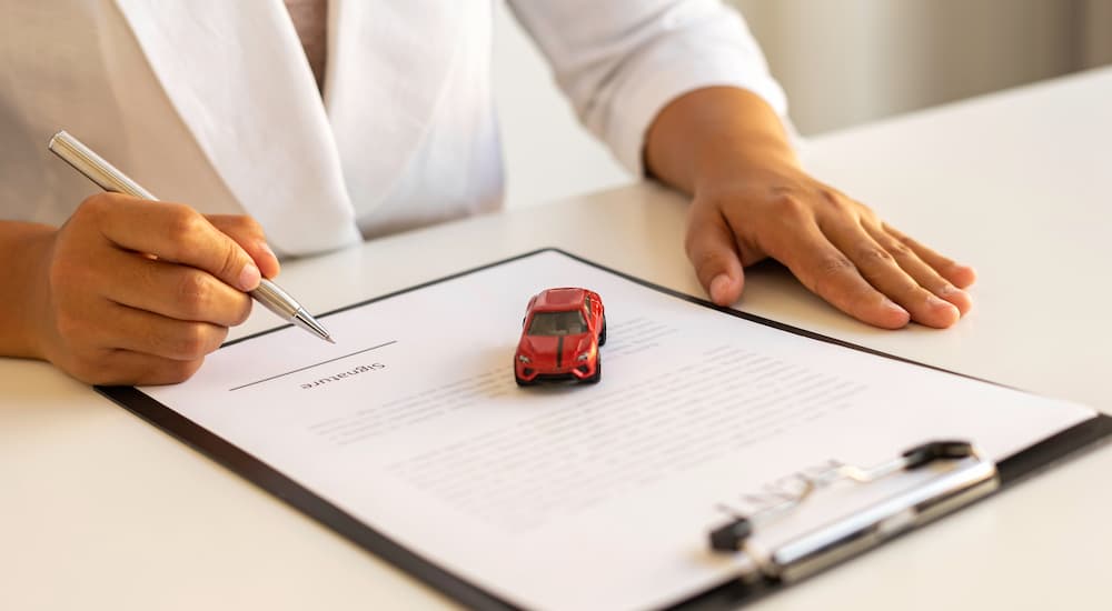 A person is shown filling out bad credit car loan paperwork at a dealership.