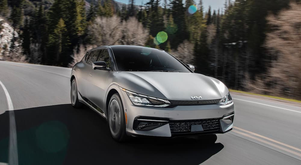 A silver 2022 Kia EV6 is shown driving on a winding road.