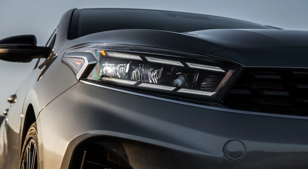 A close up of the headlight on a grey 2022 Kia Forte is shown at a car dealership.