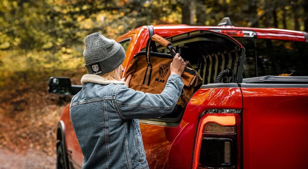 A person is shown putting a bad into the bedside compartment of a red 2022 Ram 1500.