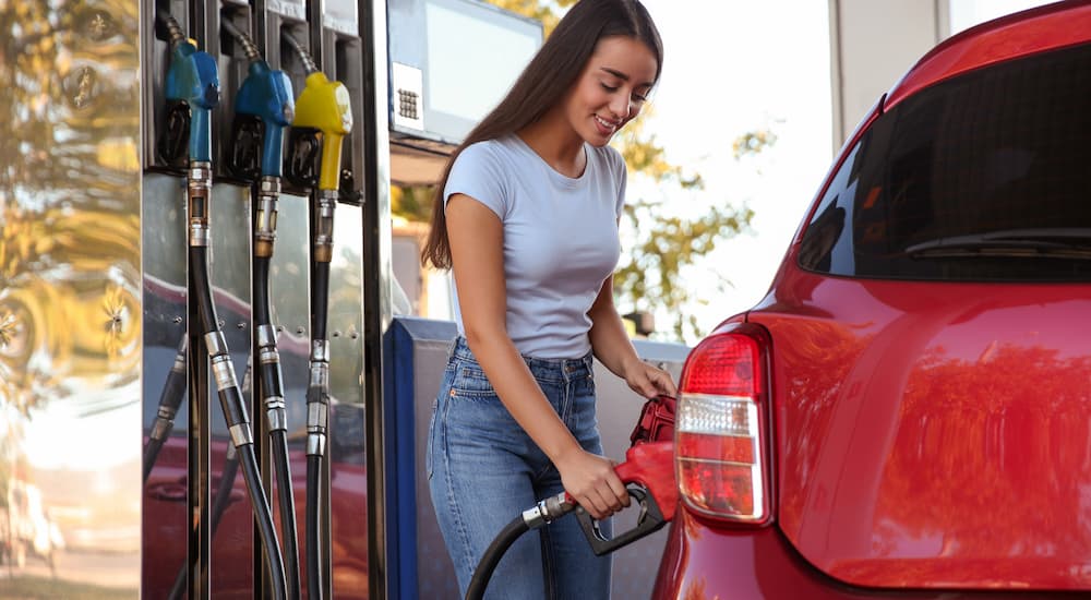 A woman is shown fueling her red car at a gas station.