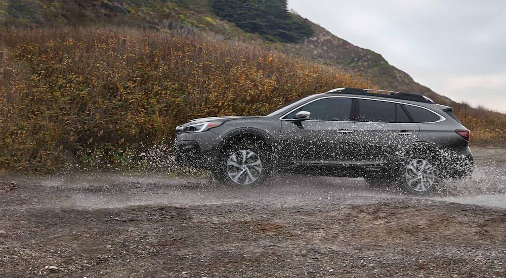 A grey 2021 Subaru Outback is shown from the side while driving through mud.