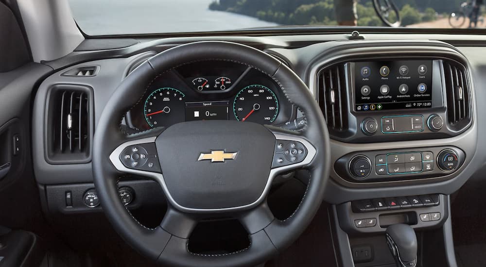 The black interior of a 2022 Chevy Colorado WT shows the steering wheel and infotainment screen.
