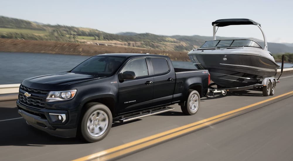 A black 2022 Chevy Colorado WT is shown towing a black boat on an open road.