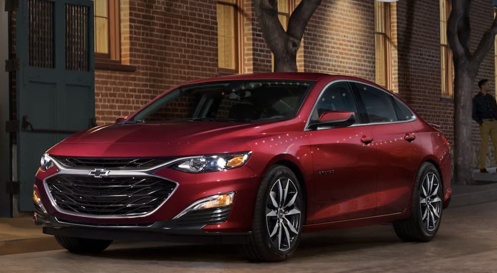 A red 2022 Chevy Malibu is shown from the side parked in front of a brick building.