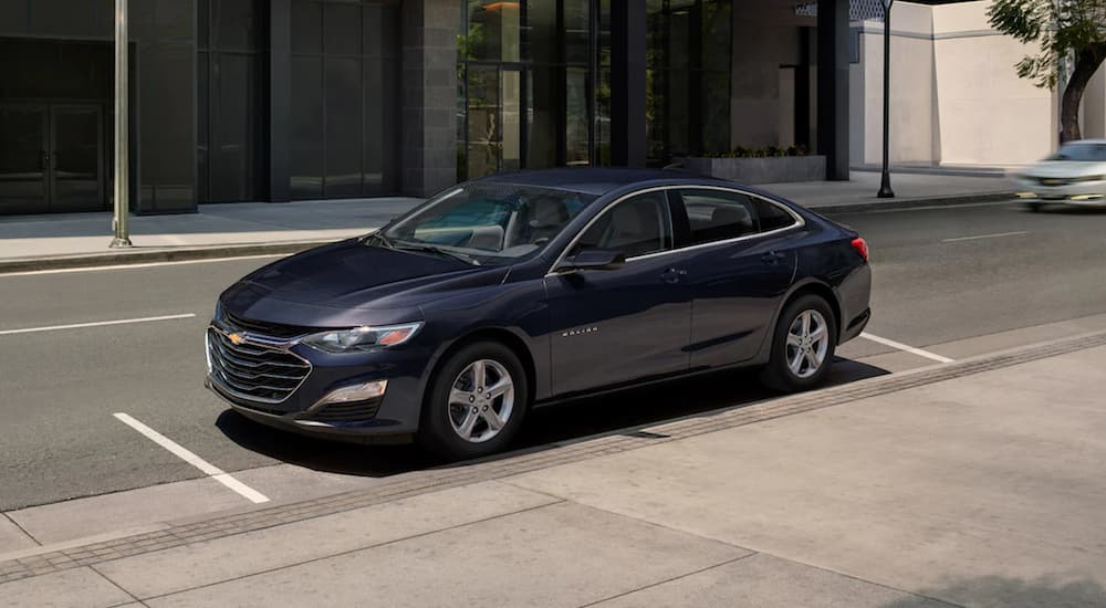 A blue 2022 Chevy Malibu is shown parked on a city street during a 2022 Chevy Malibu vs 2022 Nissan Altima comparison.