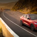 A red 2022 Ford Mustang Mach-E is shown driving on a coastal highway after winning a 2022 Ford Mach-E vs 2022 Tesla Model Y showdown.