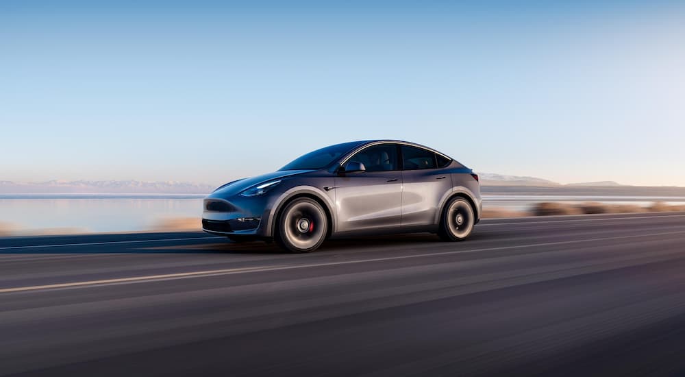 A grey 2022 Tesla Model Y is shown from the side driving past a lake.