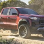 A red 2023 Chevy Colorado Trail Boss is shown from the side driving on a dirt road.