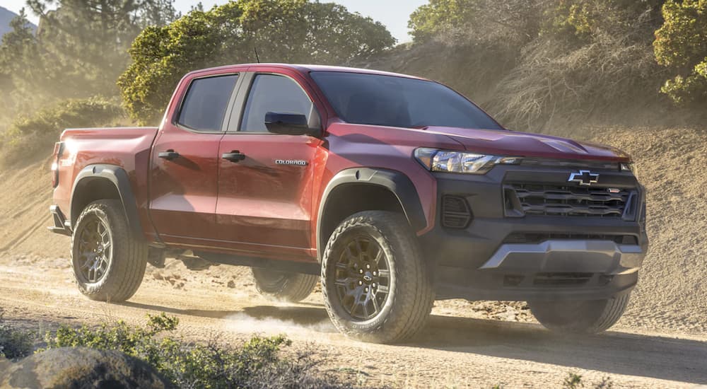 A red 2023 Chevy Colorado Trail Boss is shown from the side driving on a dirt road.