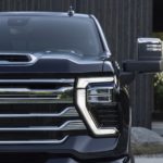 A close up shows the grille and driver side headlight on a black 2024 Chevy Silverado 2500HD High Country.