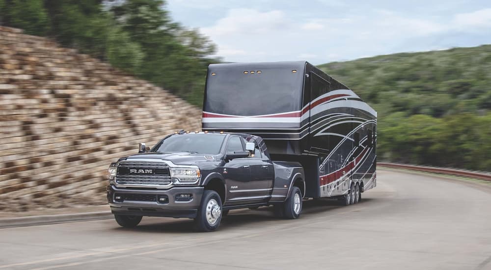 A grey 2022 Ram 3500 is shown towing a camper after leaving a Ram dealership.