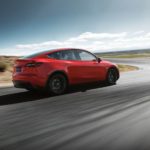 A red 2022 Tesla Model Y is shown driving on an open road.