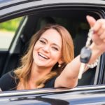 A woman is shown holding a set of car keys out of a black sedan.