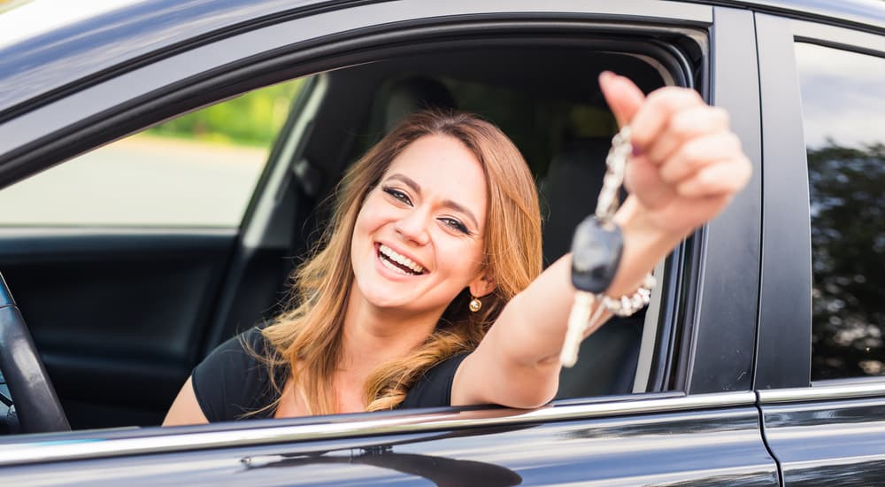 A woman is shown holding a set of car keys out of a black sedan.