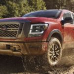 A red 2021 Nissan Titan Pro-4x is shown off-roading through a muddy river.