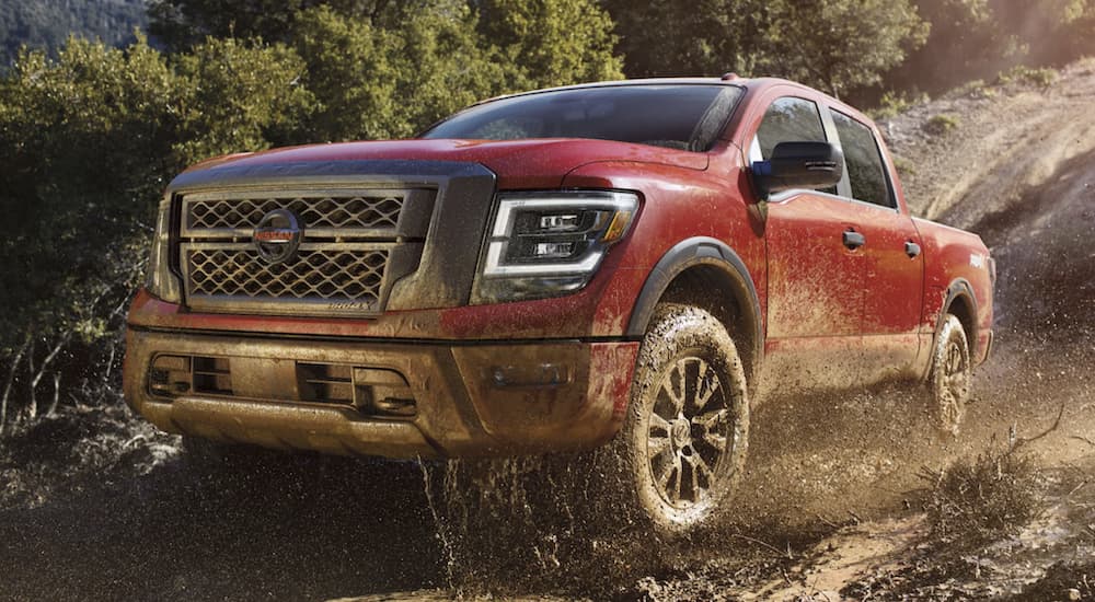 A red 2021 Nissan Titan Pro-4x is shown off-roading through a muddy river.