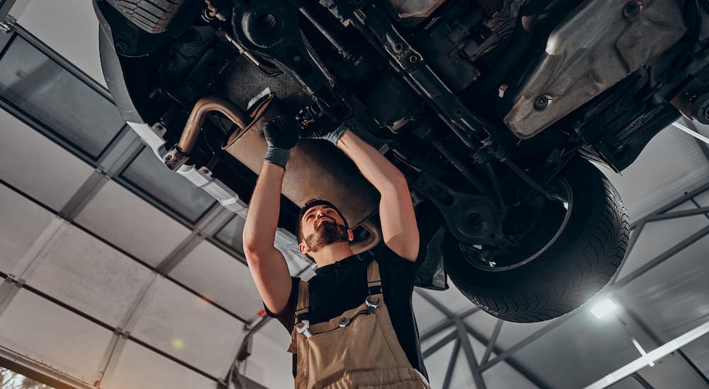 A mechanic is shown underneath a vehicle at a lifted truck dealer.