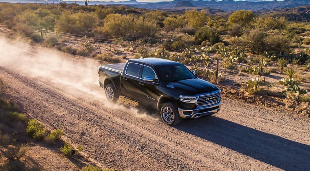 A black 2020 Ram 1500 truck for sale is shown driving on a dirt road.