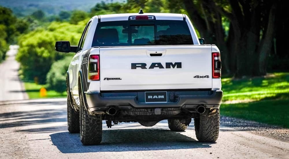 A white 2021 Ram 1500 Rebel is shown from behind driving on an open road.