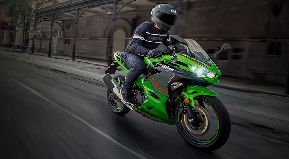 A green 2023 Kawasaki Ninja 400 is shown from the front while driving.