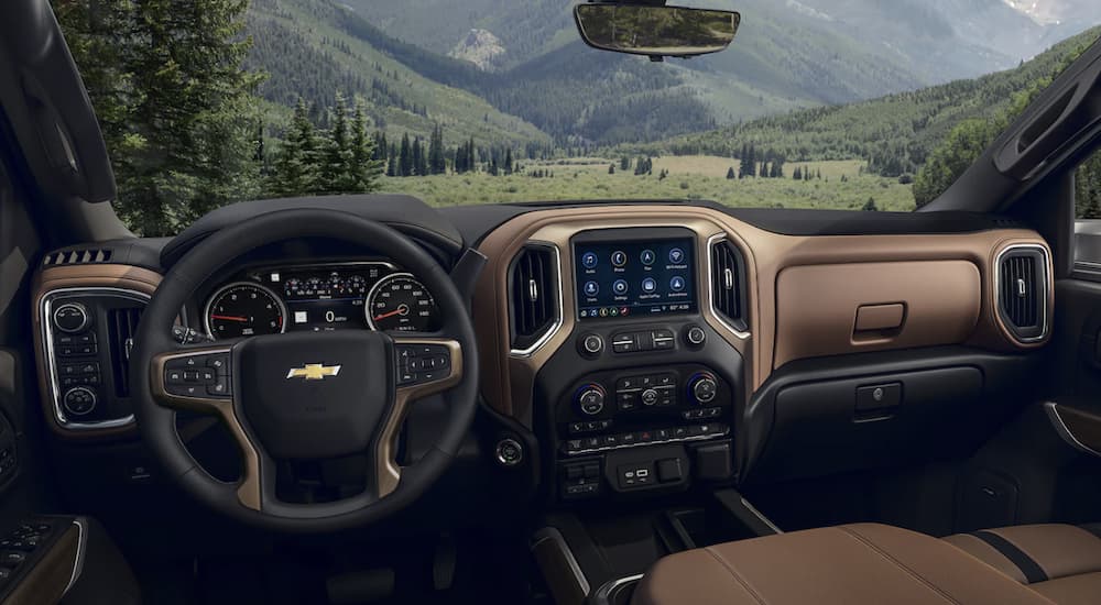 The black and brown interior of a 2023 Chevy Silverado 2500HD shows the steering wheel and infotainment screen.