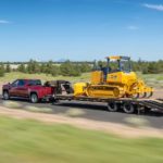 A red 2023 Chevy Silverado 3500HD is shown towing a piece of heavy equipment.