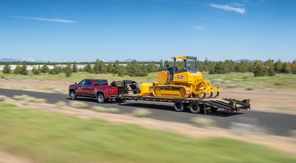 A red 2023 Chevy Silverado 3500HD is shown towing a piece of heavy equipment.