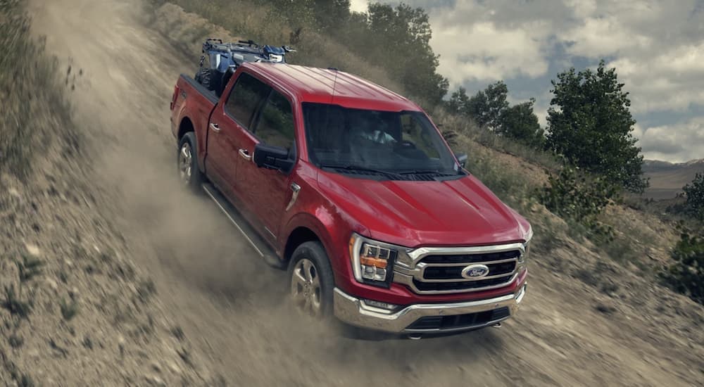 A red 2023 Ford F-150 is shown off-roading driving down a steep hill.